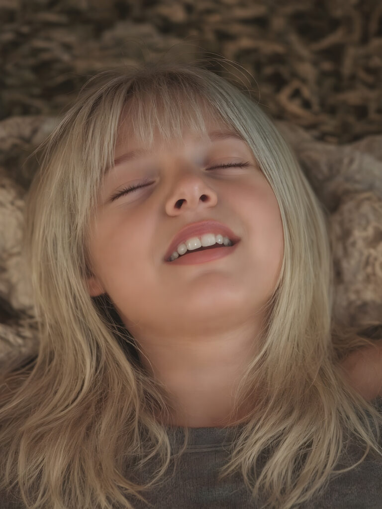 A vividly captured (((full body shot))) from a young teen girl with a warm, inviting smile, lying on the back, head tilted back, comfortably settled in a soft, inviting position. She has straight soft long blond and white hair, her (((eyes are closed))) ((wide open mouth, white teeth)) and her full lips are slightly parted, as if captured in a ((seductive moment)). The scene is set against a backdrop of a (softly lit) environment that suggests a natural, rustic setting, enhancing the warm and inviting mood of the photo.