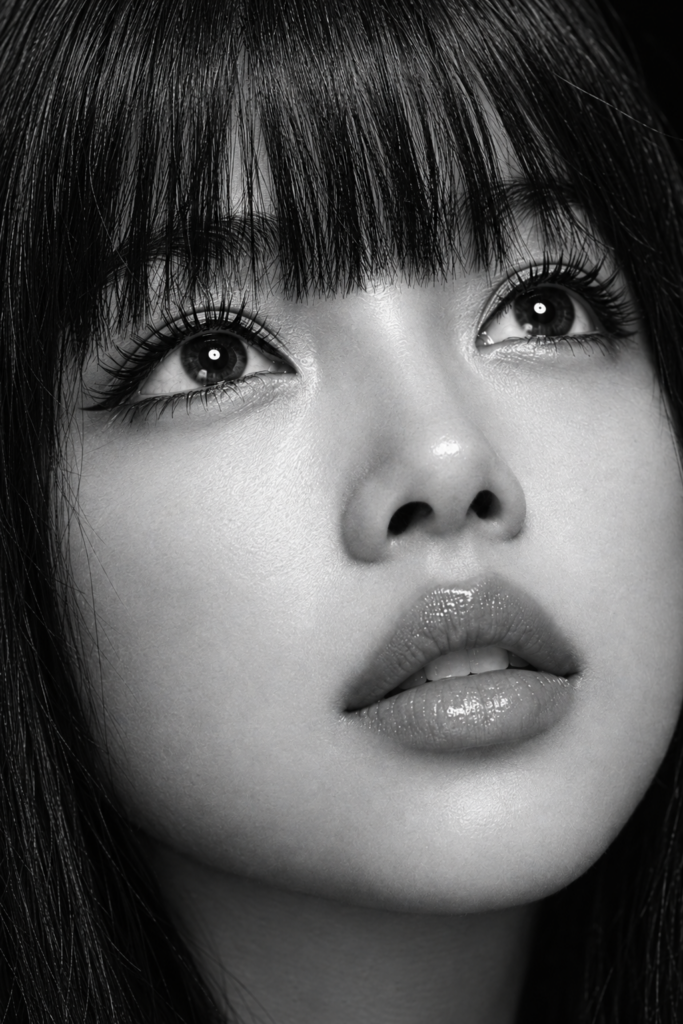 Black and white photorealistic beauty portrait of a young woman with an angelic, delicate face, flawless porcelain-smooth luminous skin, dark deep expressive eyes with long full eyelashes, full kissable lips gently parted, long straight jet-black hair with a straight fringe (bangs) falling just above her eyebrows. Very tight beauty crop from forehead to chin, she looks slightly upward past the camera, chin lifted. Tack-sharp crisp focus on the eyelashes, iris detail and lip texture, fine natural skin detail. Bright soft top light with a clean ring catchlight in the eyes, near-black background, deep blacks and silvery highlights, high-contrast monochrome. 100mm macro beauty look, editorial fashion photography, ultra detailed.