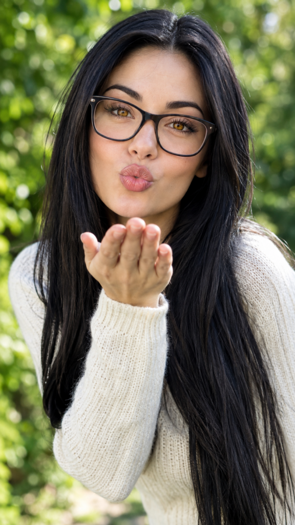 portrait from a stunningly beautiful young nerd girl, wearing a large, dark prescription glasses, age 18, with ((black long straight jet super soft hair (luminous)), flowing down to her waist, and (((bright amber eyes))), that match perfectly with her flawless complexion. She’s dressed in a tight ((wool sweater)), perfectly complemented by her (perfectly proportioned figure). Her look exudes seduction and playfulness, as she gazes directly at the viewer, all against a sunny green backdrop