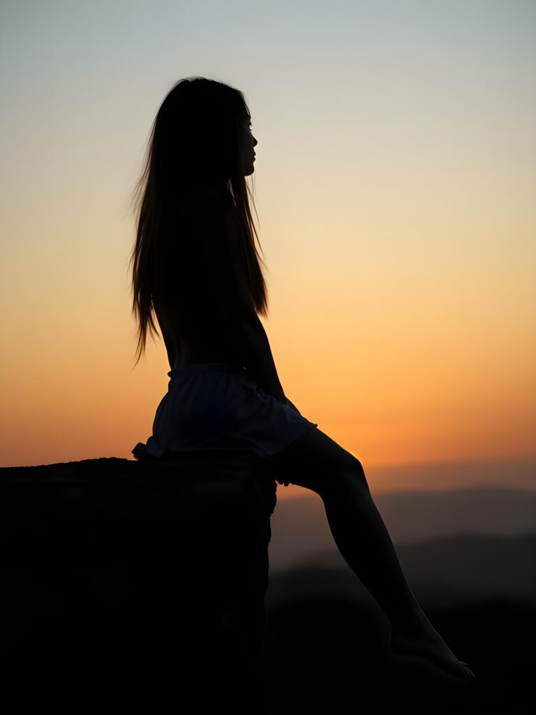 Silhouette: a girl sits on a cliff at dawn, dangling her legs. Everything is in black silhouette. Long hair falls down her back.
